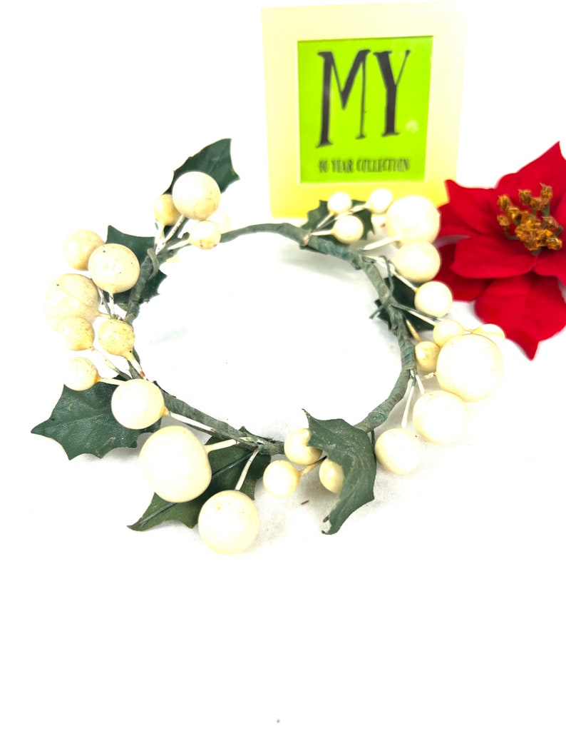 May include: A white and green artificial wreath with white berries and green leaves. The wreath is on a white background.