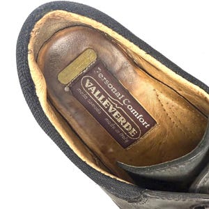 May include: Close-up of a black leather shoe with a dark brown interior. The shoe has a black fabric trim around the opening. The insole features a label with the text "Personal Comfort VALLEVERDE moda comoda made in Italy."