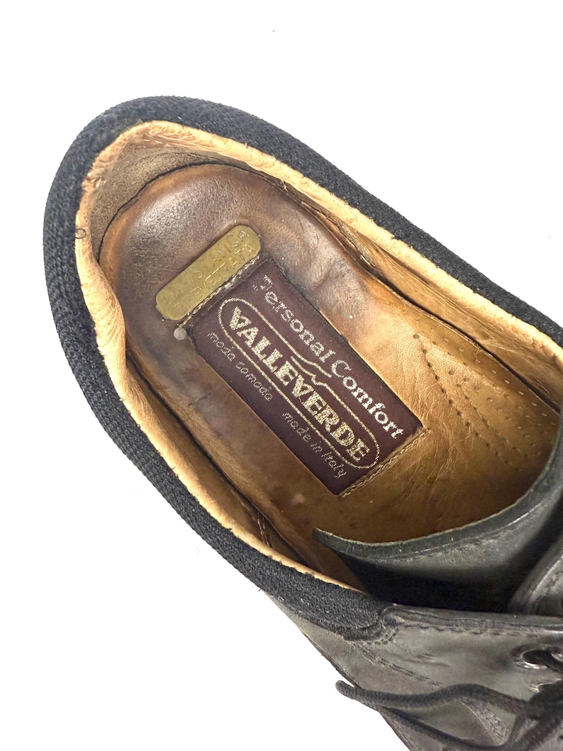 May include: Close-up of a black leather shoe with a dark brown interior. The shoe has a black fabric trim around the opening. The insole features a label with the text "Personal Comfort VALLEVERDE moda comoda made in Italy."