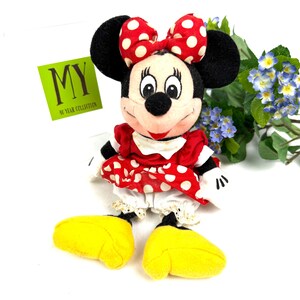 May include: A Minnie Mouse plush doll with a red and white polka dot bow, dress, and yellow shoes. The doll has black ears and a smiling face. The tag reads "MY 40 YEAR COLLECTION".