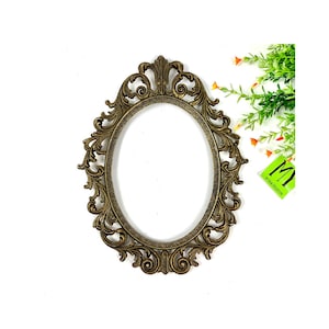May include: An ornate gold oval picture frame with a decorative, scrolled design. The frame is made of metal and has a vintage look.