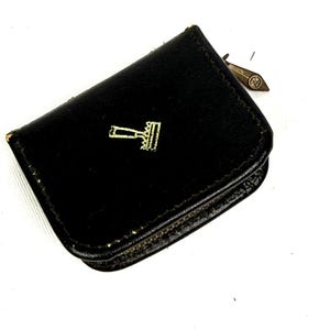 May include: Black leather coin purse with a gold-colored gavel emblem. The purse is small and rectangular with a rounded flap. A small metal tag is attached to the side. The purse is likely vintage.