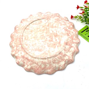 May include: A pink and white ceramic plate with a scalloped edge. The plate has a marbled design.