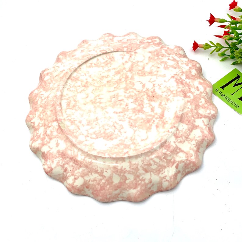May include: A pink and white ceramic plate with a scalloped edge. The plate has a marbled design.