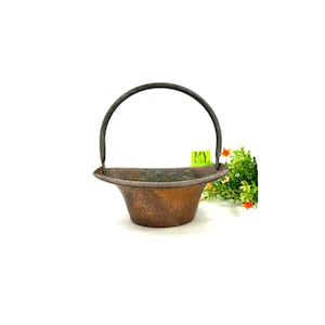 May include: A small, copper-colored planter with a hammered finish and a black metal handle. The planter is empty and has a rounded, bowl-like shape.