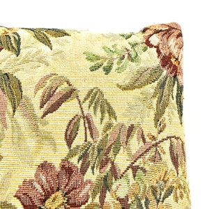 May include: A close-up of a pillow with a floral pattern. The pillow is made of a tapestry fabric with a beige background and a floral design in shades of green, brown, and red.