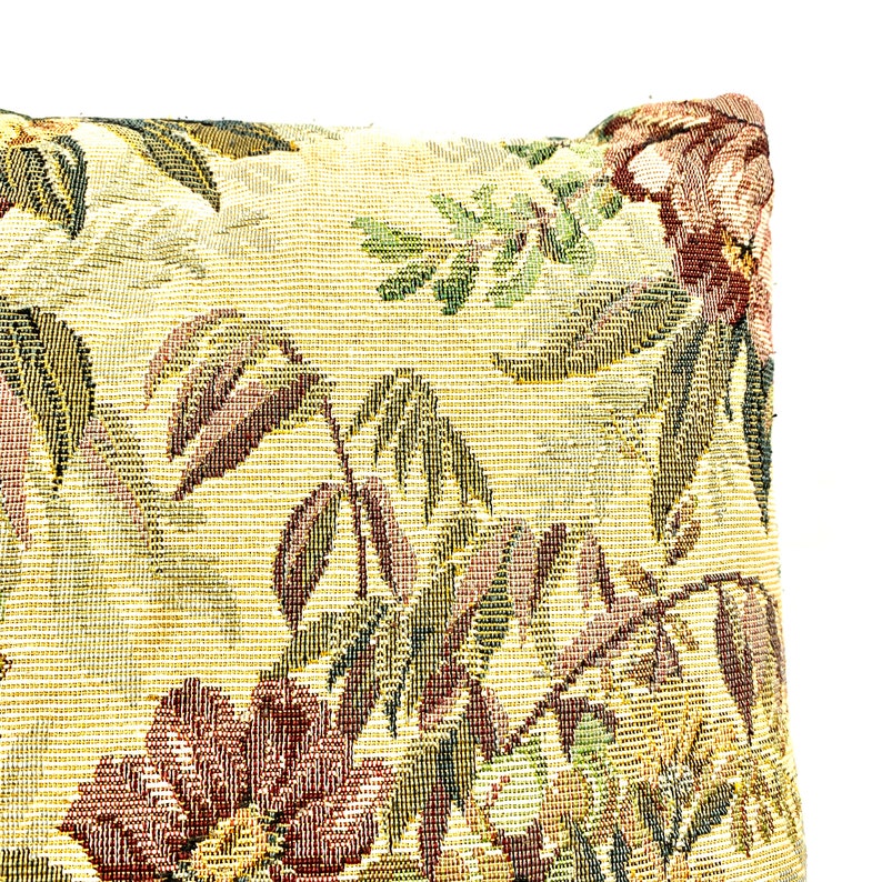May include: A close-up of a pillow with a floral pattern. The pillow is made of a tapestry fabric with a beige background and a floral design in shades of green, brown, and red.