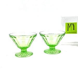 May include: Two green glass dessert bowls with a fluted design. The bowls have a pedestal base and are made of clear glass with a green tint.