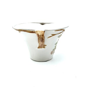 May include: White ceramic bowl with a flared rim and a textured, tree-like handle. The bowl features a brown and gold tree branch design on the side, with delicate floral accents in pink and green. The bowl has a unique, organic shape.