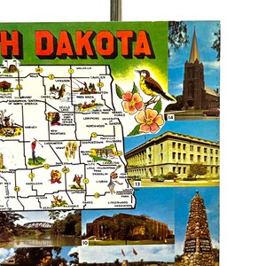May include: A vintage postcard featuring a map of North Dakota with various cities and towns highlighted. The postcard also includes images of a church, a building, and a monument.