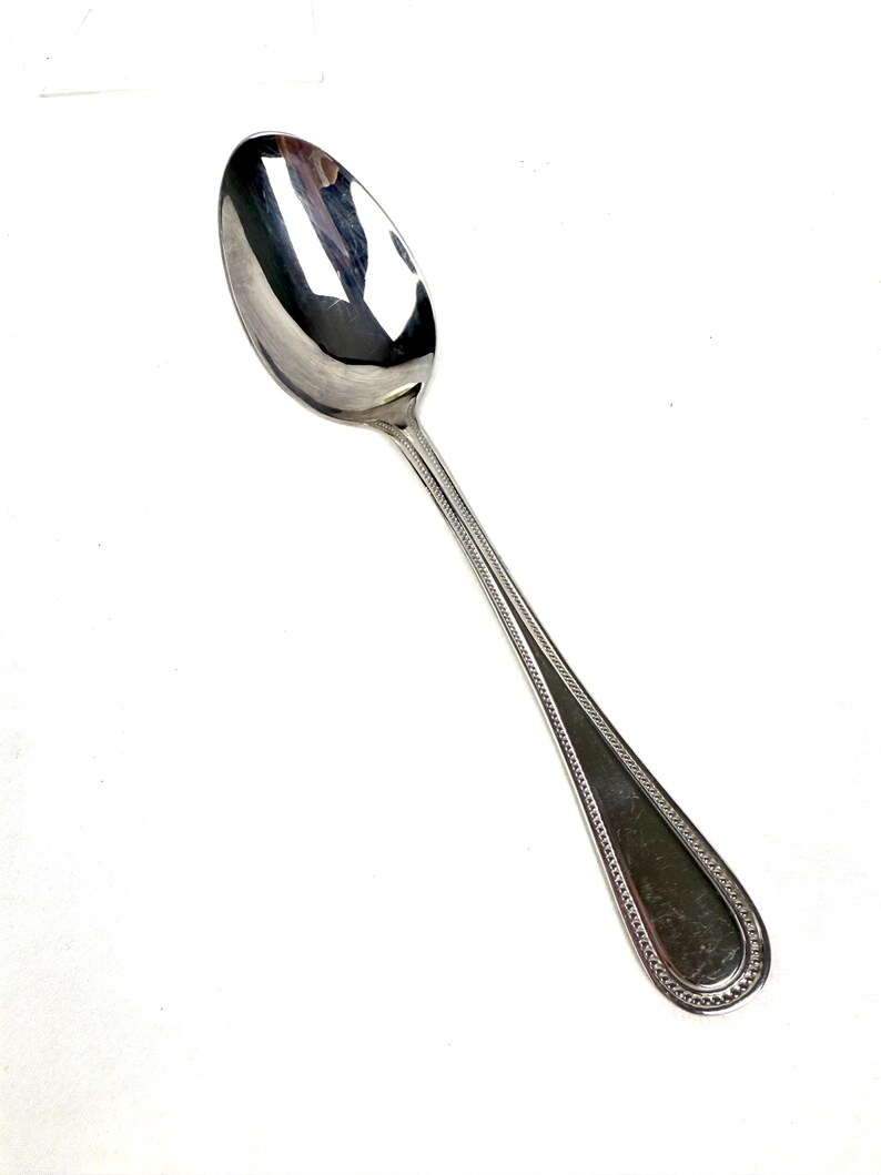 Op de afbeelding: Een zilveren lepel met een ovale kom en een lange steel. De steel heeft een decoratief randontwerp. De lepel is gemaakt van een glanzend, reflecterend metaal, waarschijnlijk roestvrij staal. De lepel staat tegen een witte achtergrond.