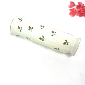 May include: White ceramic vase with a red and green floral pattern. The vase is cylindrical and has a slightly flared opening.