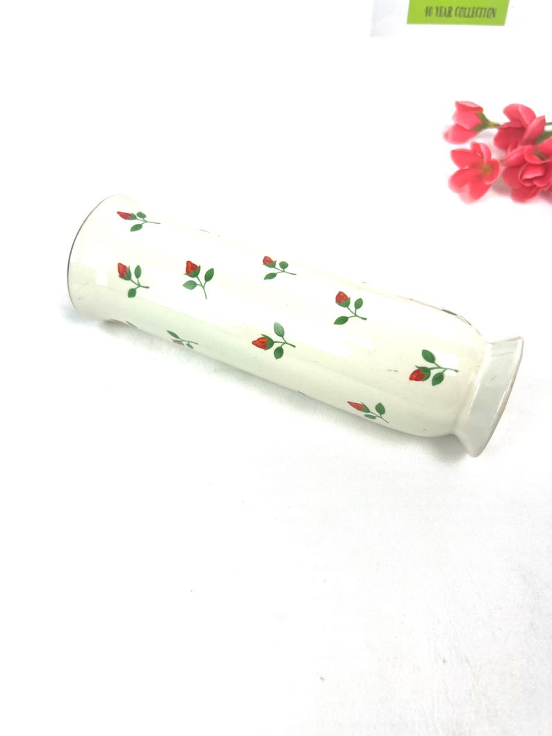 May include: White ceramic vase with a red and green floral pattern. The vase is cylindrical and has a slightly flared opening.