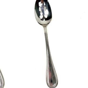 Op de afbeelding: Een zilveren serveerlepel met een sleufkom met een decoratief bloemmotief. De steel heeft een kralenrand en een druppelvormig uiteinde. De lepel is ontworpen om te serveren en is gemaakt van een glanzend, reflecterend metaal.