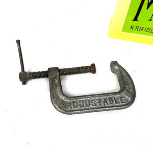 May include: A silver metal adjustable clamp with a handle and a screw. The clamp is labeled "ADJUSTABLE".