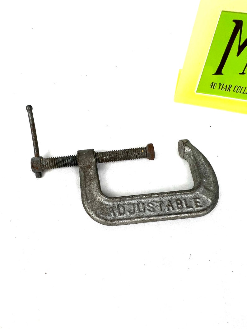 May include: A silver metal adjustable clamp with a handle and a screw. The clamp is labeled "ADJUSTABLE".