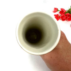 May include: The inside of a white ceramic vase. The vase is tall and narrow, with a smooth, glossy finish.