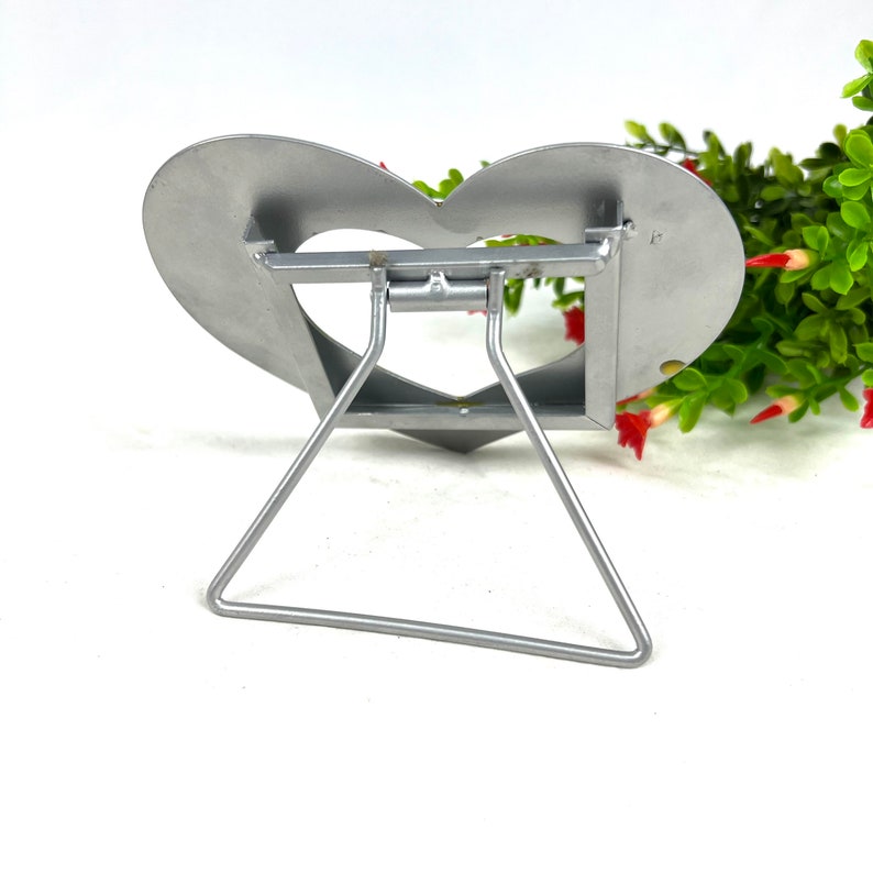 May include: Silver metal heart-shaped picture frame with a stand. The stand is a triangular shape and folds flat.
