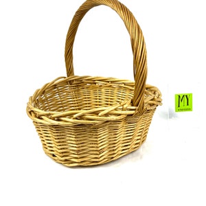 May include: A natural woven wicker basket with a rounded oval shape and a single handle. The basket is light brown in color and has a woven pattern.