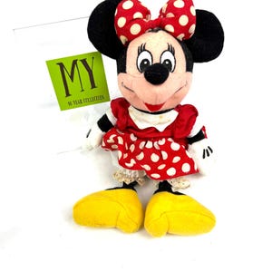 May include: A Minnie Mouse plush toy, featuring a red dress with white polka dots, a matching bow, and large yellow shoes. The toy has black ears and a tag that reads "MY 10 YEAR COLLECTION".