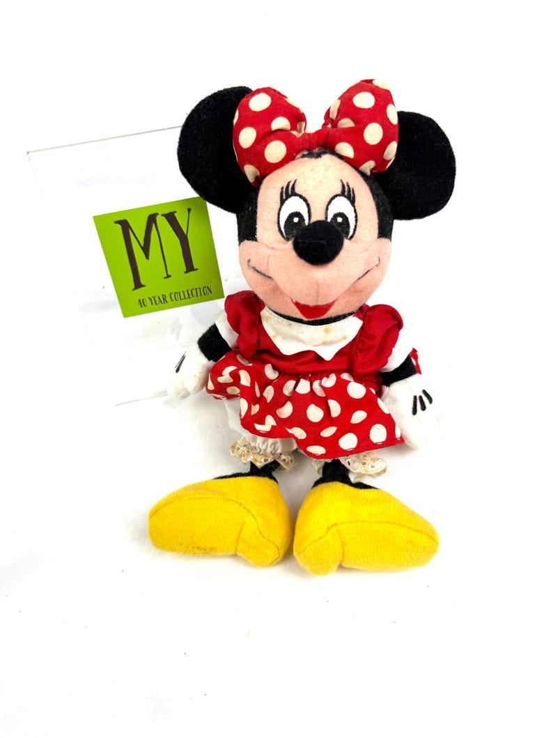 May include: A Minnie Mouse plush toy, featuring a red dress with white polka dots, a matching bow, and large yellow shoes. The toy has black ears and a tag that reads "MY 10 YEAR COLLECTION".