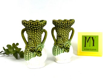 May include: A pair of green and white ceramic vases with a textured, raised design. The vases have two handles and a clover design on the bottom.