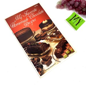 May include: A vintage cookbook titled "My Favorite Homemade Chocolate Recipes" by Violet Rutherford. The cover features a colorful display of various chocolate desserts, including cakes, pastries, and candies.