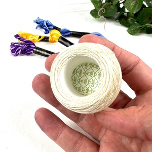 May include: A close-up of a white spool of embroidery floss with a green label that says "DMC" repeated around the edge. The label has a pattern of small diamonds and a bell.