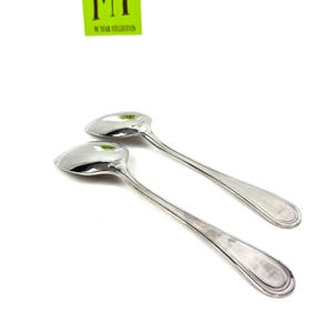 May include: Two shiny silver spoons with long, slender handles and rounded bowls. The spoons are set against a white background. The text "MY 90 YEAR COLLECTION" is in a green rectangle in the upper left corner.