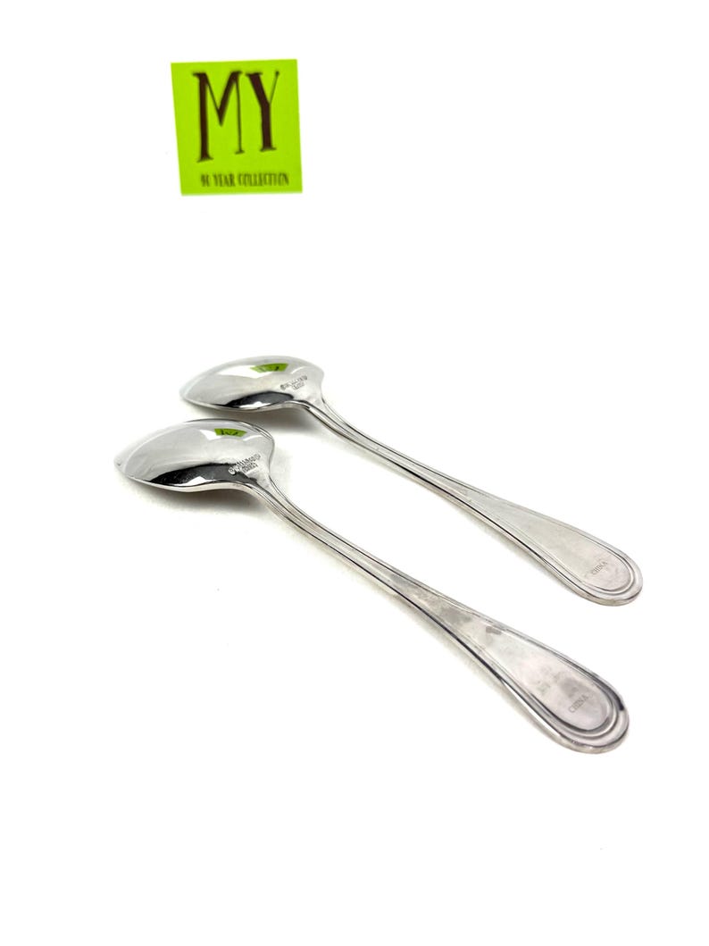 May include: Two shiny silver spoons with long, slender handles and rounded bowls. The spoons are set against a white background. The text "MY 90 YEAR COLLECTION" is in a green rectangle in the upper left corner.