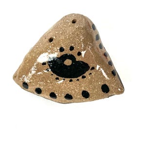 Könnte beinhalten: Ein handgefertigtes, braunes Keramik-Salz- und Pfefferstreuer-Set. Die dreieckigen Streuer haben eine gesprenkelte Textur und sind mit schwarzen Punkten und einem schwarzen augenartigen Design verziert. Das Set hat mehrere Löcher zum Ausgeben.