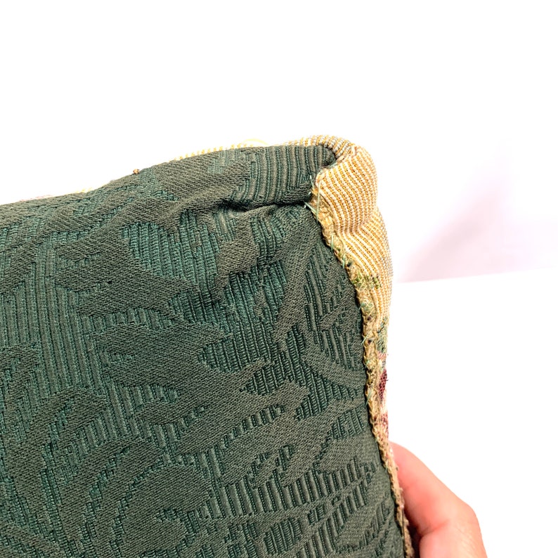 May include: Close-up of the corner of a green and beige patterned throw pillow. The pillow has a textured fabric with a subtle floral design.