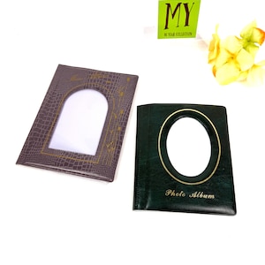 Peut inclure: Deux albums photo. L'un est marron fonc&eacute; avec une ouverture photo rectangulaire et un motif d&eacute;coratif dor&eacute;. L'autre est vert fonc&eacute; avec une ouverture photo ovale et les mots "Photo Album" en or. Un panneau vert indique "MY 10 YEAR COLLECTION".