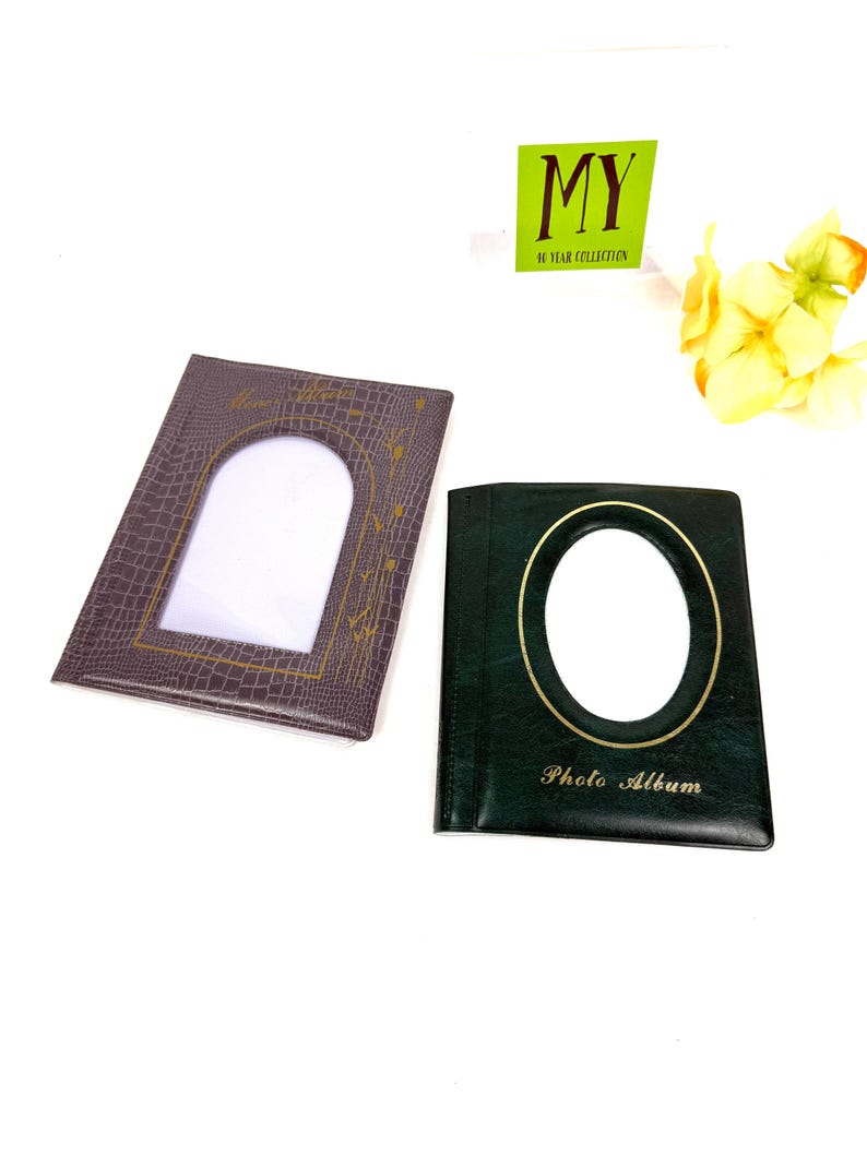 Peut inclure: Deux albums photo. L'un est marron fonc&eacute; avec une ouverture photo rectangulaire et un motif d&eacute;coratif dor&eacute;. L'autre est vert fonc&eacute; avec une ouverture photo ovale et les mots "Photo Album" en or. Un panneau vert indique "MY 10 YEAR COLLECTION".