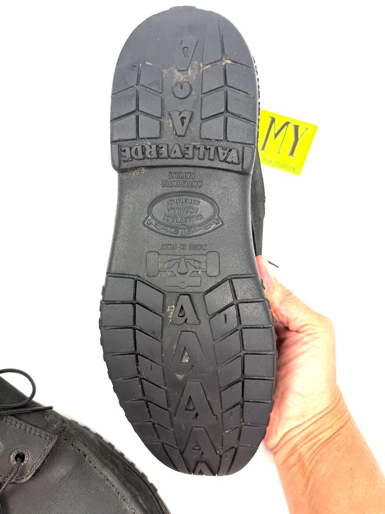 May include: Black work boot with a textured sole. The sole features the brand name "VALLEVERDE", "ANTISTATIC", and "MADE IN ITALY". The boot is held by a hand against a white background.