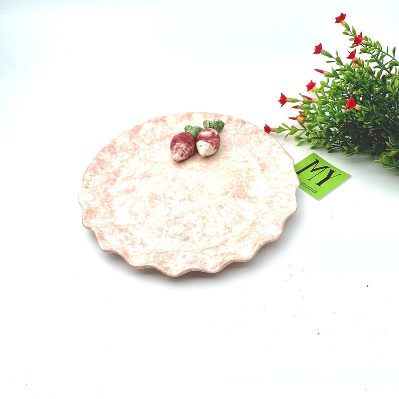May include: A pink ceramic plate with a scalloped edge and a white and pink marbled design. Two small ceramic radishes are on the plate.