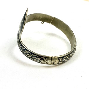 May include: A silver bangle bracelet with a black enamel design. The bracelet has a hinged clasp and a decorative end piece.