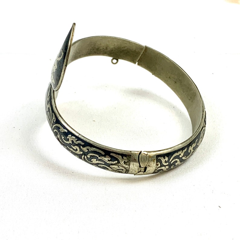 May include: A silver bangle bracelet with a black enamel design. The bracelet has a hinged clasp and a decorative end piece.