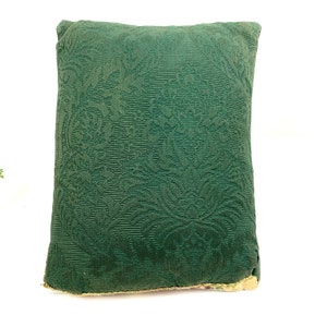 May include: A green throw pillow with a floral damask pattern. The pillow is made of a soft, textured fabric.