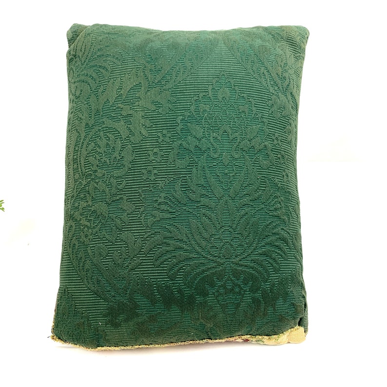 May include: A green throw pillow with a floral damask pattern. The pillow is made of a soft, textured fabric.