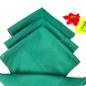 May include: Four green linen napkins folded in a stack. The napkins have a subtle striped pattern and a white border.