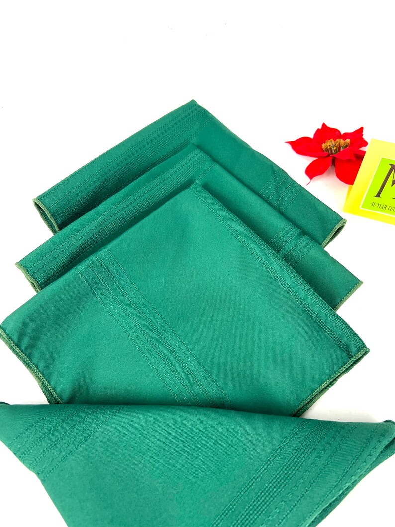 May include: Four green linen napkins folded in a stack. The napkins have a subtle striped pattern and a white border.