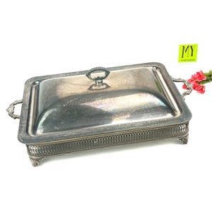 May include: Silver serving dish with a lid and ornate feet. The dish has a decorative border and a handle on the lid.