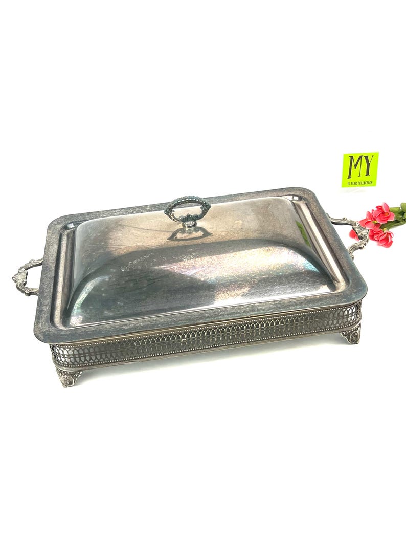 May include: Silver serving dish with a lid and ornate feet. The dish has a decorative border and a handle on the lid.