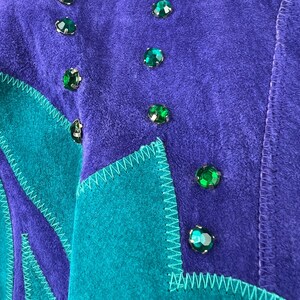 May include: A purple and teal suede jacket with green rhinestone embellishments. The jacket has a geometric design with a zig-zag stitch detail.