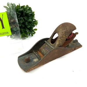 May include: A vintage metal hand plane with a rusty finish and a red plastic adjustment knob. The plane has a wooden base and a metal blade.