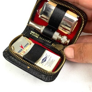 May include: A vintage black leather travel shaving kit with a zipper, red lining, and silver-toned razor. The kit includes a razor, blades, and the text "CASE MADE IN AUSTRIA LEATHER".