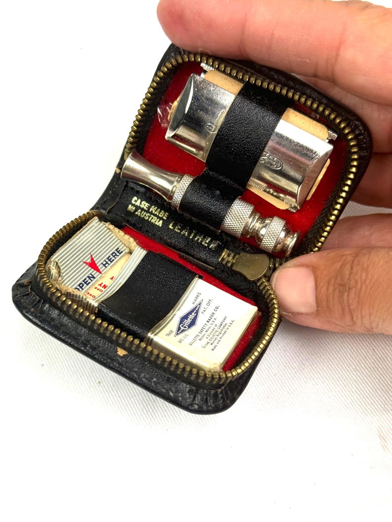 May include: A vintage black leather travel shaving kit with a zipper, red lining, and silver-toned razor. The kit includes a razor, blades, and the text "CASE MADE IN AUSTRIA LEATHER".