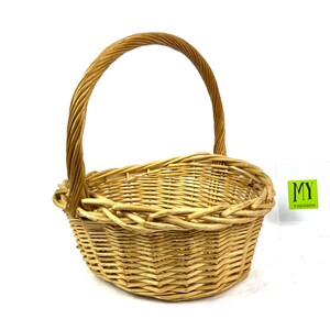 May include: A natural woven wicker basket with a rounded oval shape and a single handle. The basket is made of light brown wicker and has a natural, rustic look.