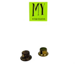May include: Two small, metallic, hat-shaped objects. One is a tarnished brown, the other is gold. The objects are on a white background. A green square with the text "MY" and "40 YEAR COLLECTION" is in the background.